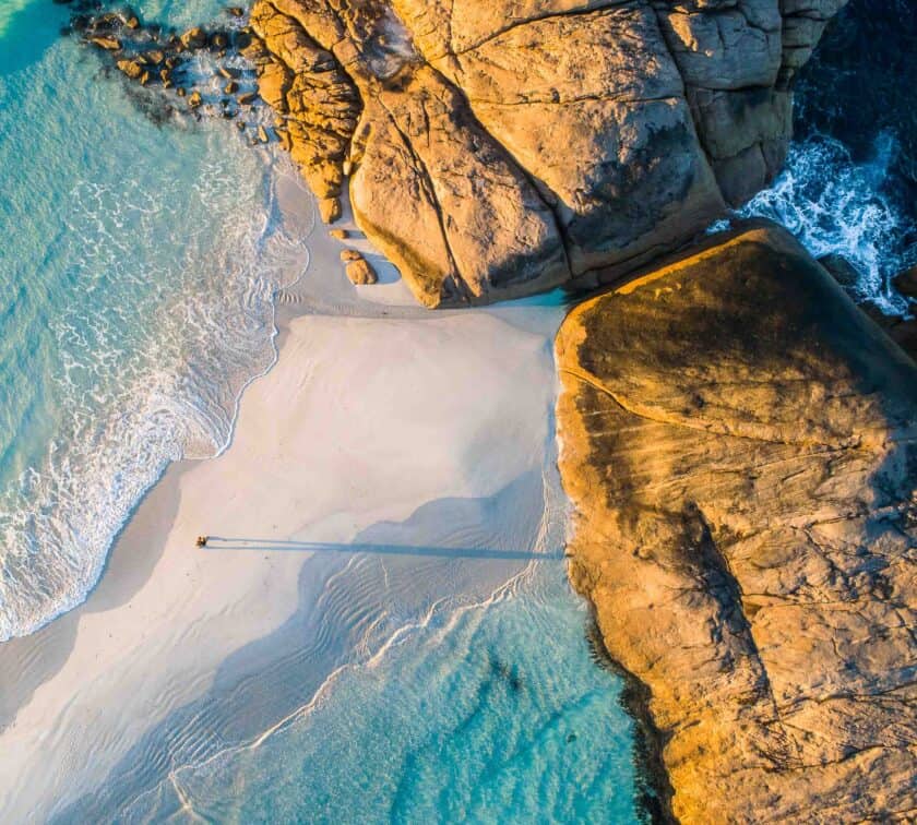 Coastline aerial view of the ocean and a man walking along white sandbar beach.